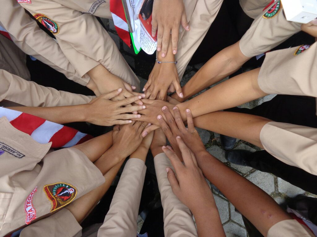 Top view crop anonymous ethnic female servicewomen in military uniforms joining hands while standing on paved street